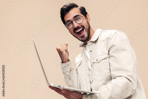 Portrait of a stylish man smile with teeth with a laptop in the hands of a freelancer, on a beige background in a white t-shirt, fashionable clothing style, space space