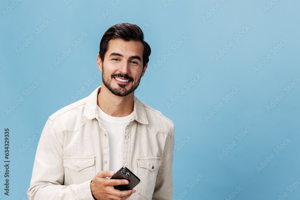 Portrait of a brunette man with a phone in his hands smiling on a blue background in a white T-shirt and jeans, copy space Portrait of a brunette man with a phone in his hands smiling on a blue background in a white T-shirt and jeans, copy space