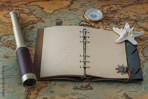 Open leather book with blank pages for writing text or a logo, a spyglass, a starfish and a brass compass lie on a vintage map