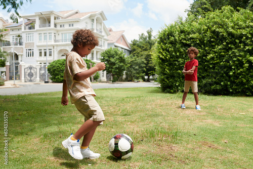 Brothers playing soccer after school on green meadow