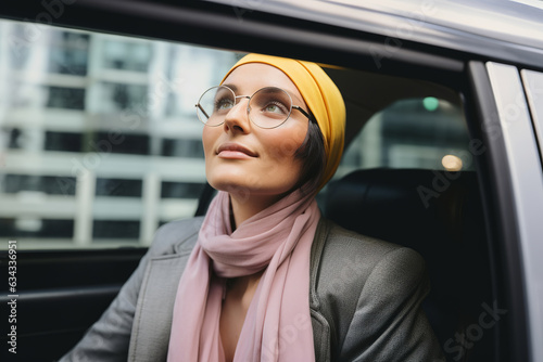 Young businesswoman in yellow headscarf and glasses sitting in the car and looking through window away.