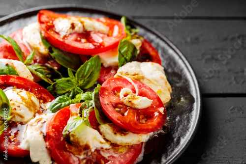 Delicious caprese salad with ripe tomatoes, mozzarella cheese and fresh basil leaves on dark wooden boards. Close up