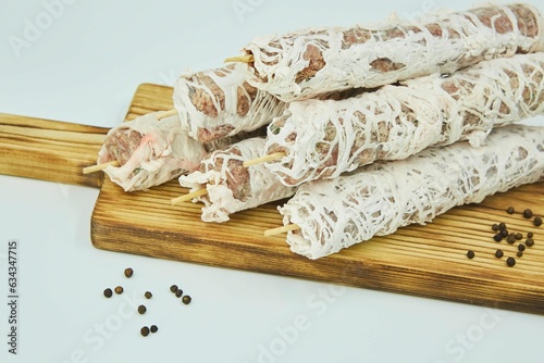 Meat wrapped in a fat mesh lies on a wooden board. Raw product. The dish lyulya is a kebab. White background. photo