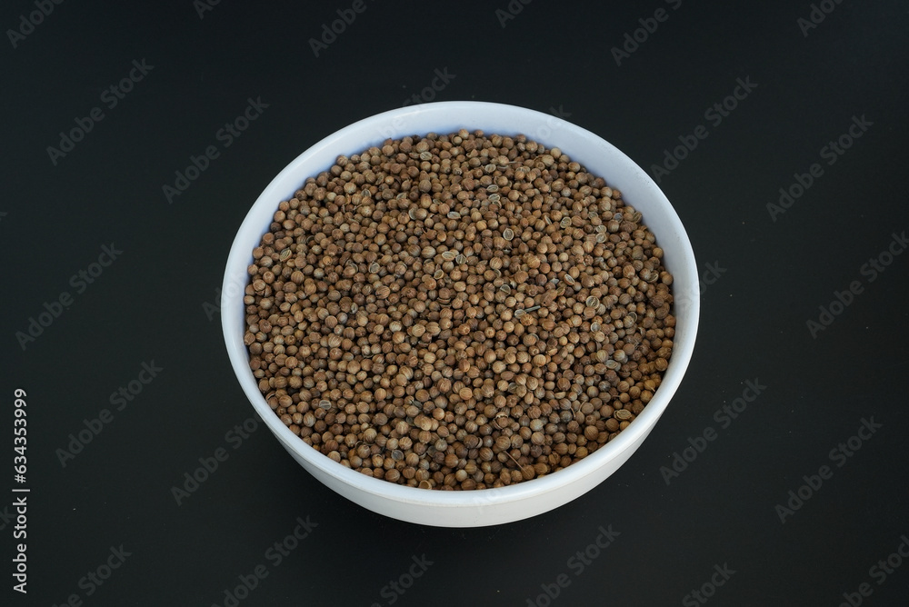 coriander seeds in a white plate on a black background coriander seeds in a white plate on a black background
