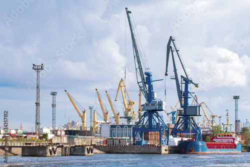 Sea cargo harbor. Port with cranes on shore. Harbor for loading ships. Container port on sunny day. Cargo harbor in summer weather. Export across ocean. Maritime logistics. Cargo transportation