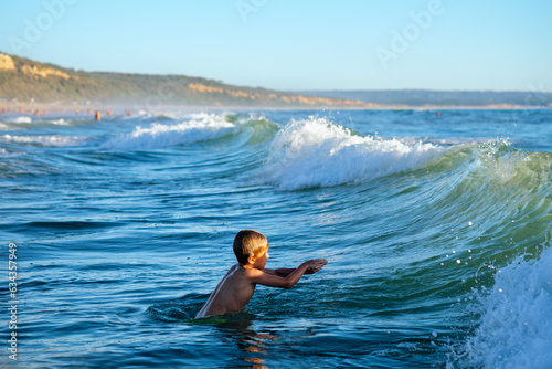 Boy has fun enjoys jumps dives in ocean sea waves of Atlantic Ocean. Fonta da Telha beach, Costa da Caparica, Portugal photo