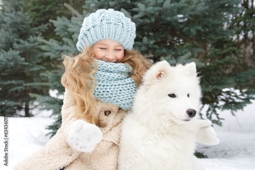 Little beautiful girl, cute happy positive child kid is lying on snow, play, having fun with her big white dog at winter day in park or forest © Евгений Шемякин