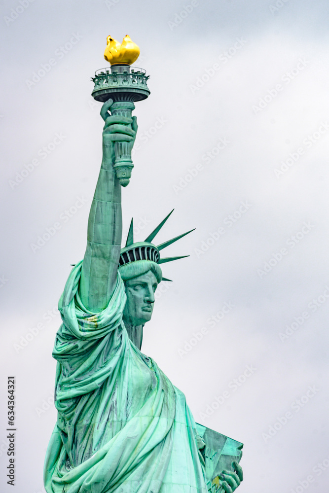 Fototapeta premium New York, New York, United States. August 07, 2023. Dramatic and detailed image of the Statue of Liberty with strong shades of green, sky with many clouds and very high resolution.