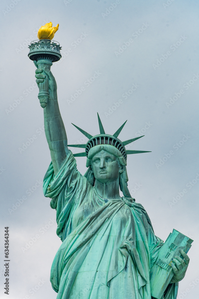 Fototapeta premium New York, New York, United States. August 07, 2023. Dramatic and detailed image of the Statue of Liberty with strong shades of green, sky with many clouds and very high resolution.