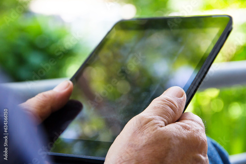 Senior man sitting outside reading E-book on his tablet.