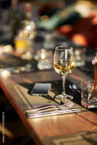 A glass of white wine is on the table. A glass of wine and a mobile phone on a table in a restaurant. 
