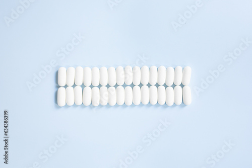 Lot of medicine pills on blue background. Scattered white pills on blue table. 