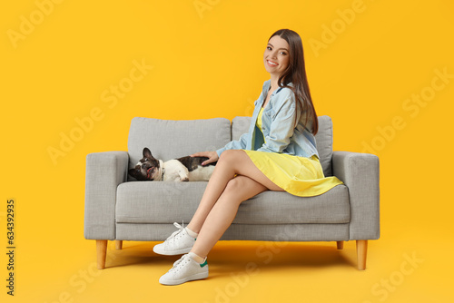 Young woman with her French bulldog on sofa against yellow background