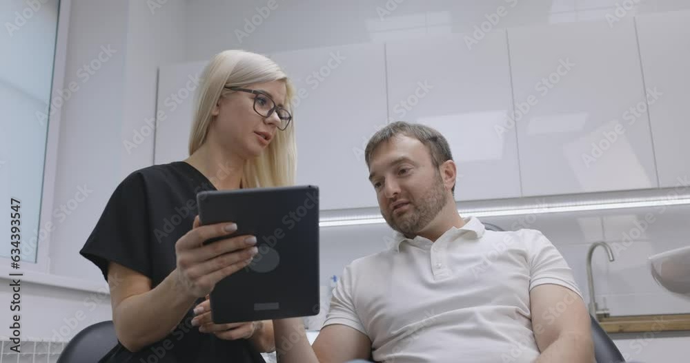 A dentist girl looks at a photo of teeth on a tablet together with a man and discusses a further treatment plan A dentist girl looks at a photo of teeth on a tablet together with a man and discusses a further treatment plan