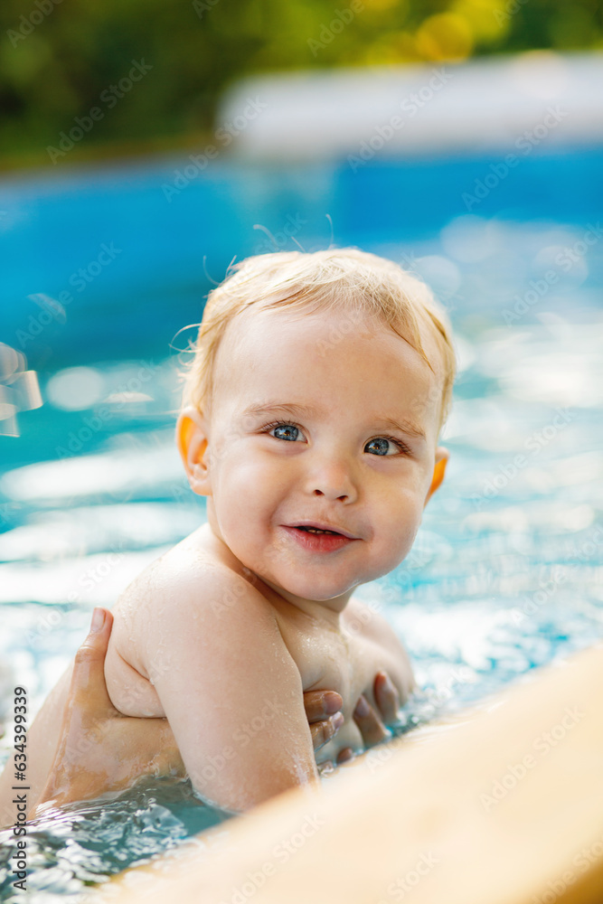 Portrait of small red-haired boy bathes in pool with hand support, baby swimming in water, summer leisure Portrait of small red-haired boy bathes in pool with hand support, baby swimming in water, summer leisure