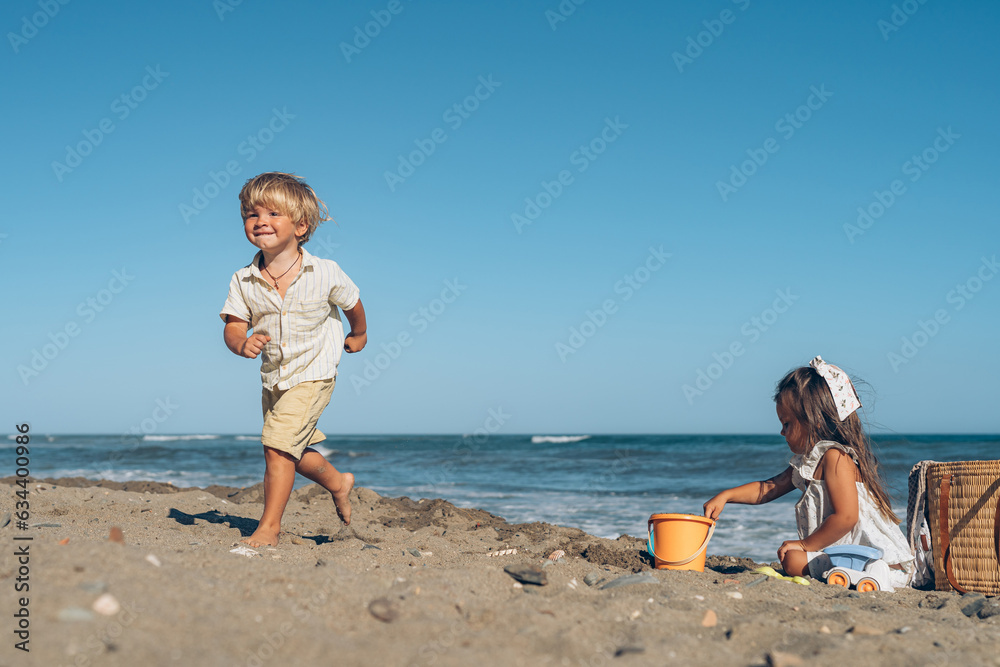 a little boy and a girl of three years old play in the sand on the beach near the sea a little boy and a girl of three years old play in the sand on the beach near the sea