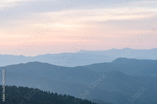 multiple mountain range ridges of decreasing contrast and clarity due to haze as they get further away from the lens, the vanilla sky facing away fron the sunset is calm and peaceful yet cloudy 