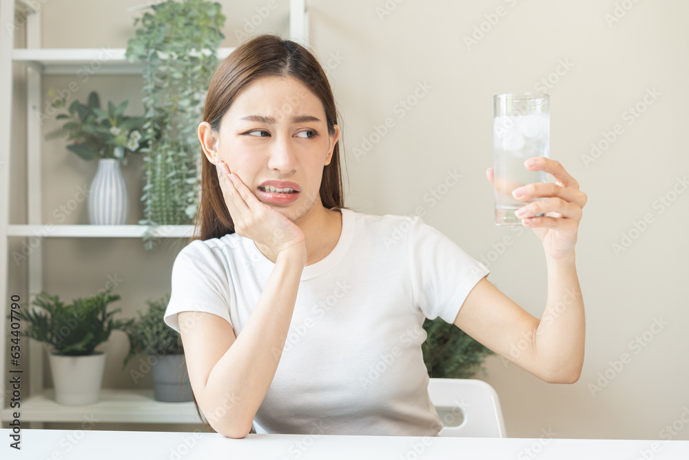 Suffering from toothache, blur asian young woman touch cheek, face expression ache or feel pain, sensitive molar teeth, hand holding glass of water with ice, inflammation when drink cold, healthcare. Suffering from toothache, blur asian young woman touch cheek, face expression ache or feel pain, sensitive molar teeth, hand holding glass of water with ice, inflammation when drink cold, healthcare.