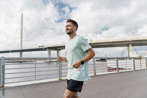 Runner trainer in fitness clothes T-shirt, running sports shoes and smart watch for sports. A strong man. A confident male athlete training does warm-up exercises.