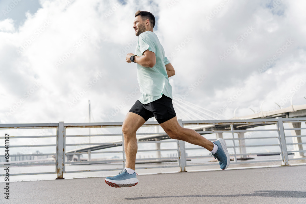 Motivation a male trainer who is training does warm-up exercises. Mental health of a person.   Uses a sports watch to measure heart rate. A runner in full-length fitness clothes, running shoes.