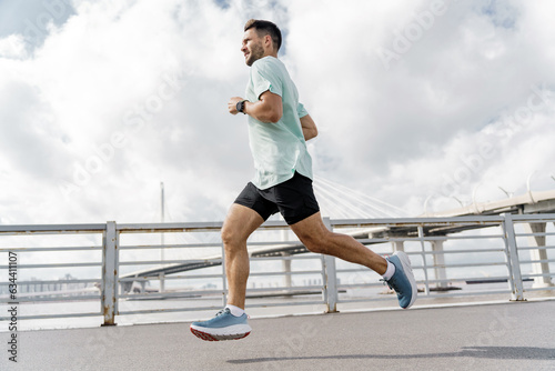 Motivation a male trainer who is training does warm-up exercises. Mental health of a person.   Uses a sports watch to measure heart rate. A runner in full-length fitness clothes, running shoes. © muse studio