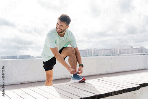 A confident person. Runner trainer in fitness clothes T-shirt, running sports shoes and smart watch. Motivation a male athlete training does warm-up exercises.