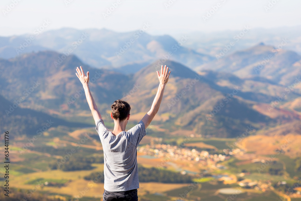 Man on top of the mountain feeling happy with arms raised while contemplating the beautiful view of mountains. Concept of happiness and mental well-being