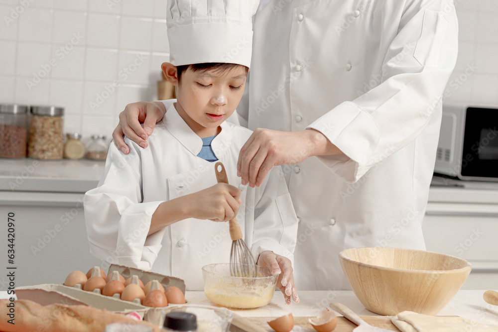 Happy Asian son and father in chef uniform with hat cook meal together at kitchen, dad parent and boy child mixing and kneading bread dough, cute family making bakery. Kid student learns to bake bread Happy Asian son and father in chef uniform with hat cook meal together at kitchen, dad parent and boy child mixing and kneading bread dough, cute family making bakery. Kid student learns to bake bread