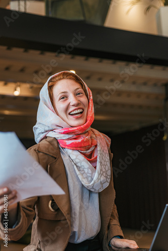 Cheerful muslim female entrepreneur in hijab holding document and smiling