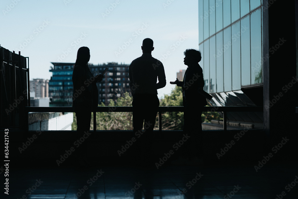 Silhouette of three business investors discussing new project during outdoor meeting in modern city area