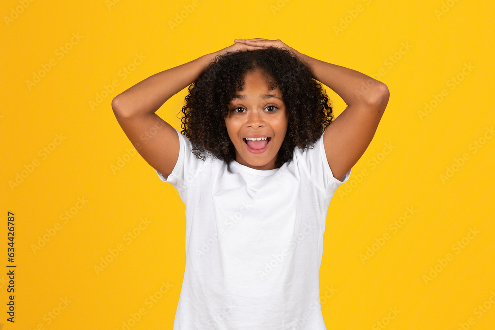 Glad shocked teenage black schoolgirl in white t-shirt with open mouth, isolated on yellow background Glad shocked teenage black schoolgirl in white t-shirt with open mouth, isolated on yellow background