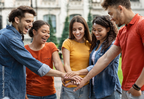 Multiracial group of students joining hands together while standing outdoors