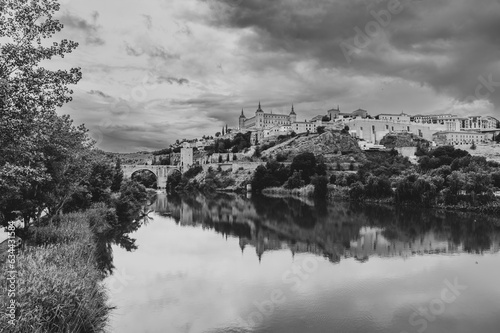 Black and white view of the Spanish city of Toledo, a UNESCO World Heritage Site, with the Tagus river and the Alcazar, under a threatening stormy sky