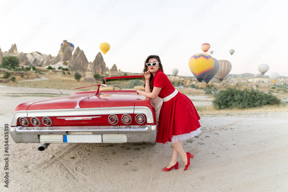 beautiful girl in retro style posing near a vintage red cabriolet car on background of balloons in Cappadocia. - obrazy, fototapety, plakaty 