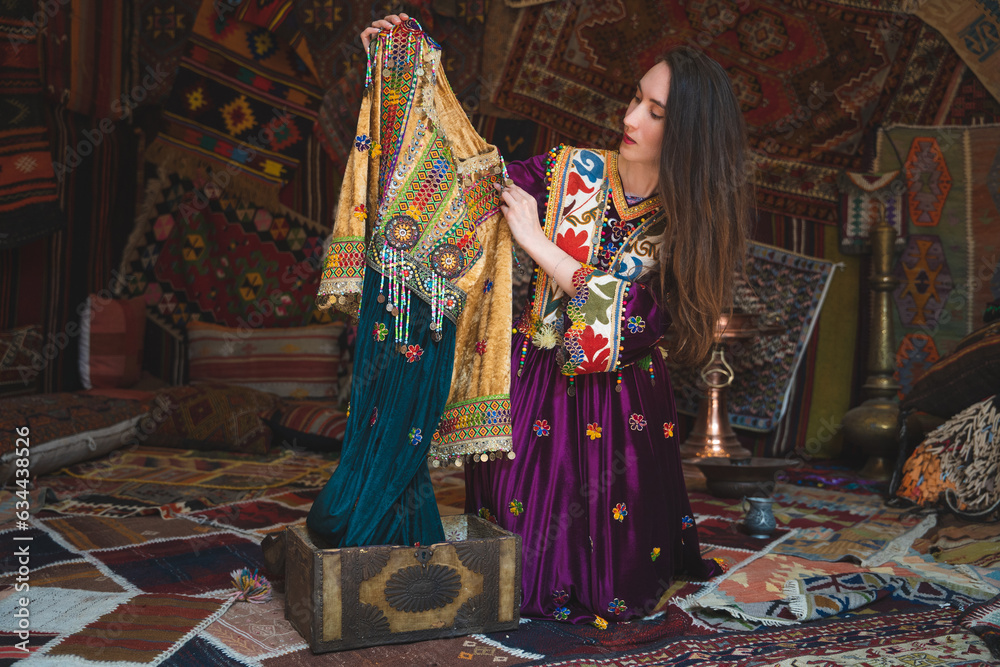 beautiful girl dressed in Turkish national clothes in the room with the interior there are many carpets on the walls