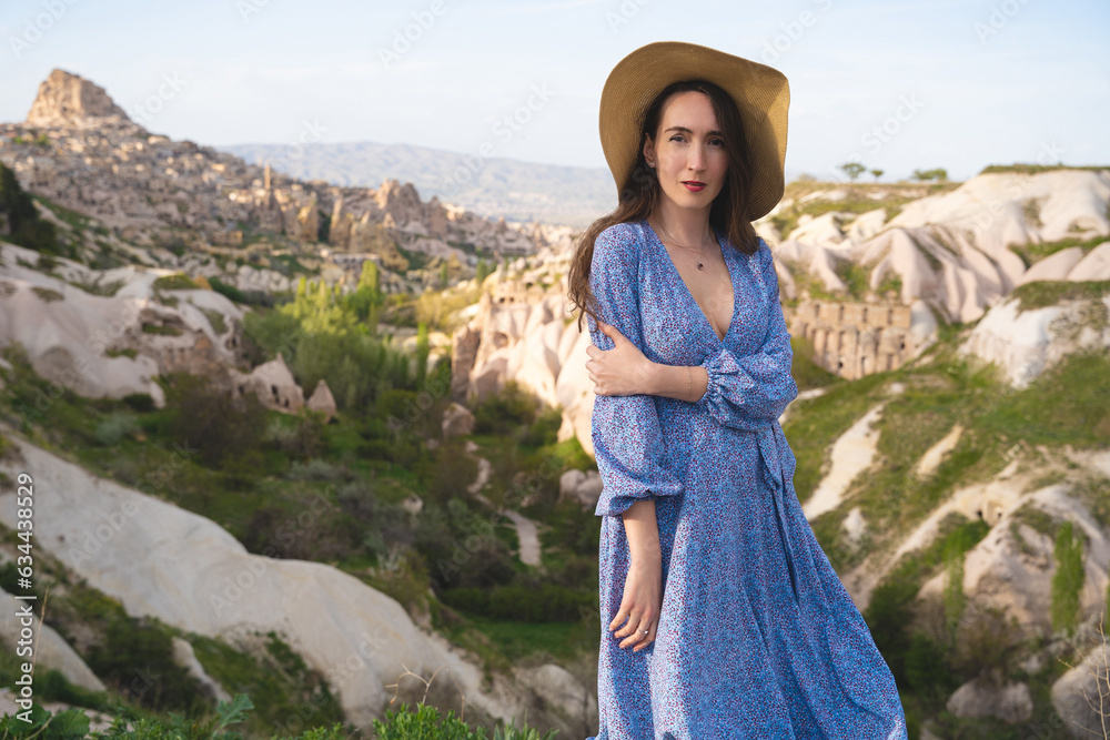 a beautiful girl in a dress and hat is enjoying the mountain landscape in Cappadocia