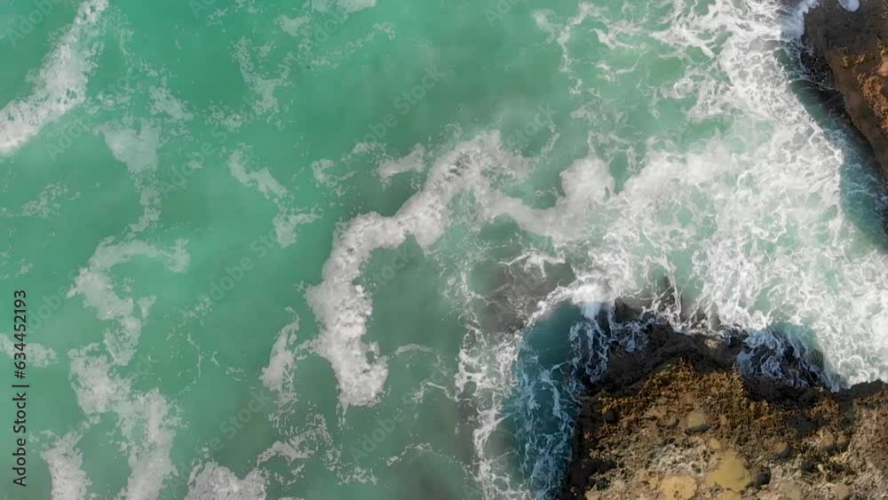 Rocks against ocean waves, overhead super slow motion view from drone