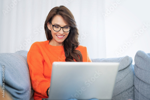 Attractive woman sitting on the sofa at home and using laptop for work