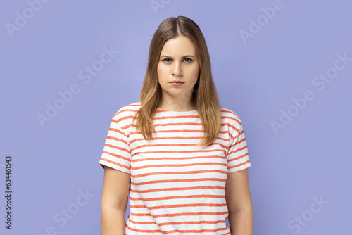 Portrait of blond woman wearing striped T-shirt being upset of bad news, looking at camera with frowning face, expressing sadness. Indoor studio shot isolated on purple background.
