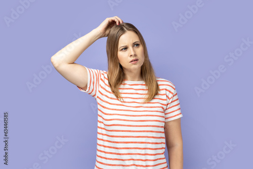 Portrait of clever thoughtful blond woman wearing striped T-shirt thinking over startup idea, pondering smart strategy, doubting decision. Indoor studio shot isolated on purple background.