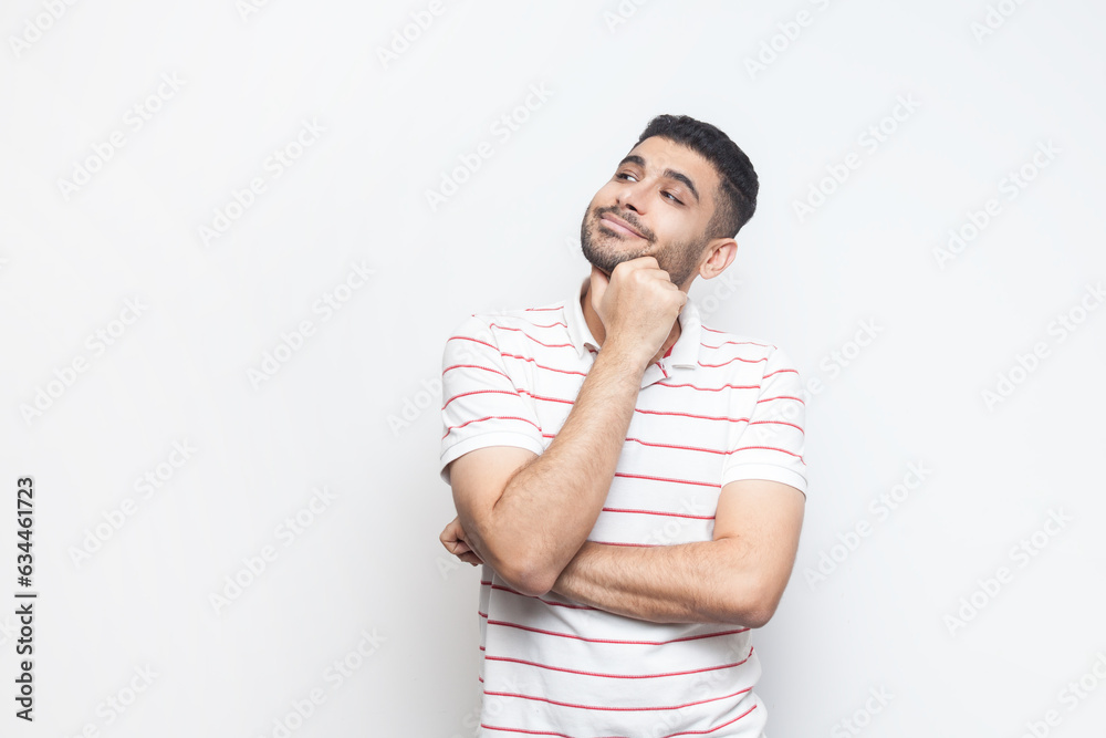 Portrait of pensive dreaming positive bearded man wearing striped t-shirt standing looking away, thinking about something pleasant. Indoor studio shot isolated on gray background. Portrait of pensive dreaming positive bearded man wearing striped t-shirt standing looking away, thinking about something pleasant. Indoor studio shot isolated on gray background.