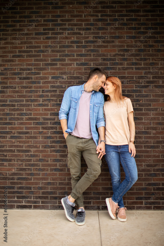 Smiling young couple in love in front of house brick wall