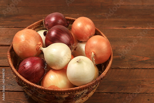 Various varieties of onions in a basket on a wooden background, autumn harvest concept, red, white and golden onions for breeding in agriculture, selective focus