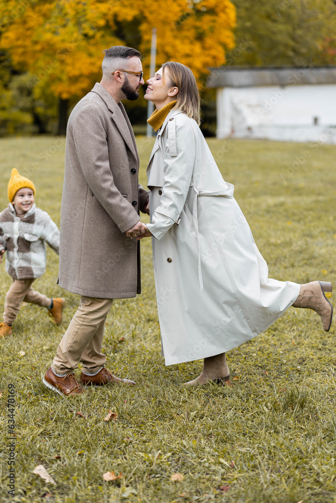 Fototapeta premium Happy family on a beautiful fall picnic in the park. Cozy autumn vibes. Young father, mother and their cute sn spending quality time together, having fun.