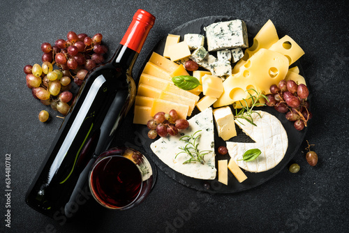 Cheese platter with craft cheese assortment on slate board and red wine at black background. Top view.