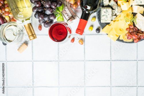 Cheese platter with wine glasses. Craft cheese assortment on slate board at white tile background. Top view with copy space.
