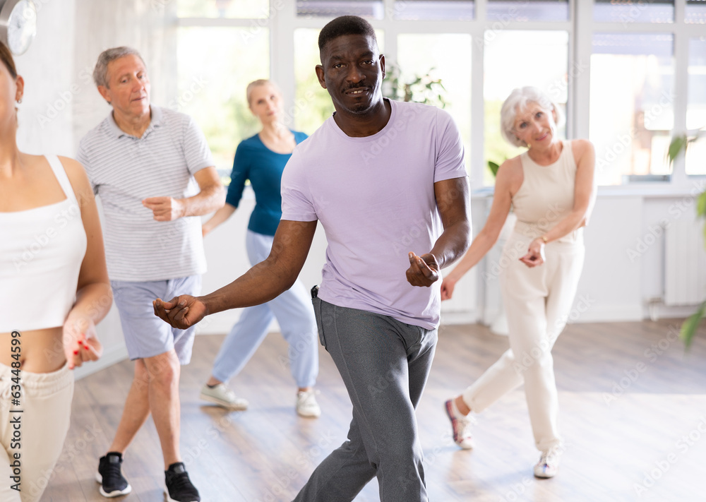 Fototapeta premium African American man is engaged in modern dance class with group friends of different age and learn to perform movements to rhythmic music.