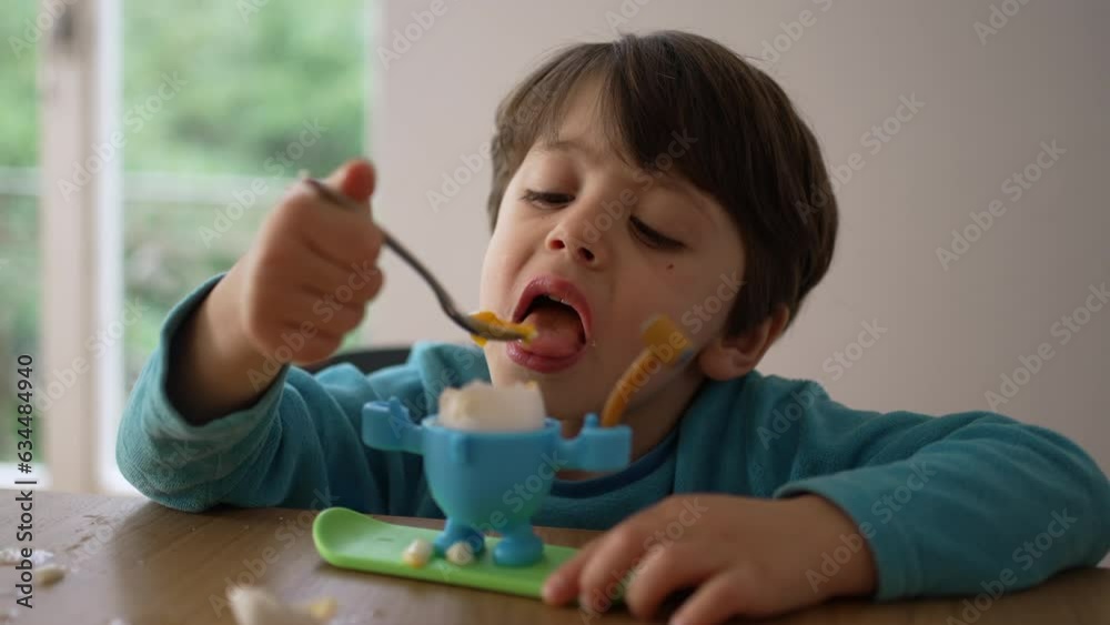Child eating soft boiled egg for breakfast with spoon. 4 year old little boy eating by himself, close-up face absorbed in healthy snack, oeuf a la coque Child eating soft boiled egg for breakfast with spoon. 4 year old little boy eating by himself, close-up face absorbed in healthy snack, oeuf a la coque