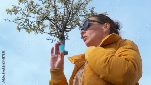 Woman with asthma against sky. A view of sick female use an inhaler against clear blue sky. photo