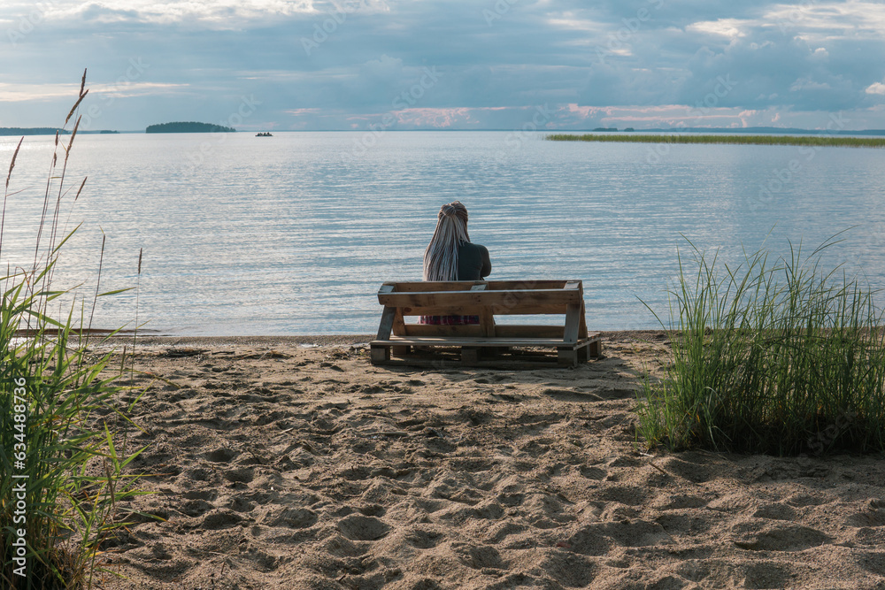 woman traveler with de braids hairstyle sitting on a bench made of old pallets on a sandy shore of a vast lake woman traveler with de braids hairstyle sitting on a bench made of old pallets on a sandy shore of a vast lake